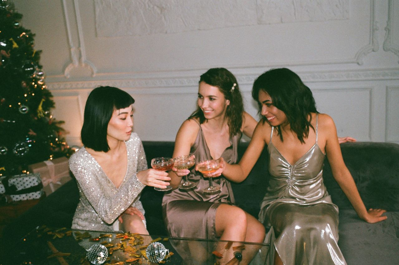 Mastering the First Impression: Your intriguing post title goes here Three friends in glamorous dresses sharing drinks at a festive indoor gathering.