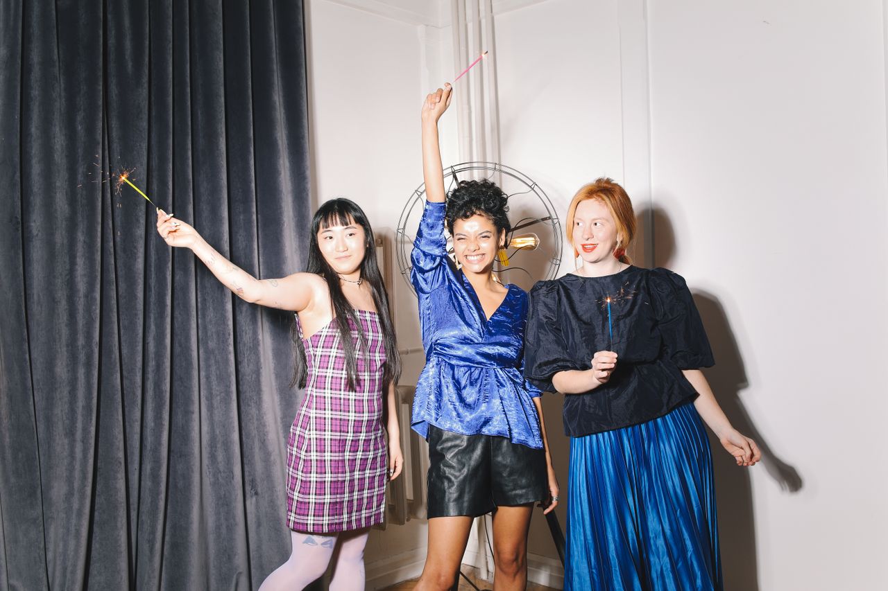 services-01 Three women joyfully celebrating indoors with sparklers, showcasing diverse fashion styles.
